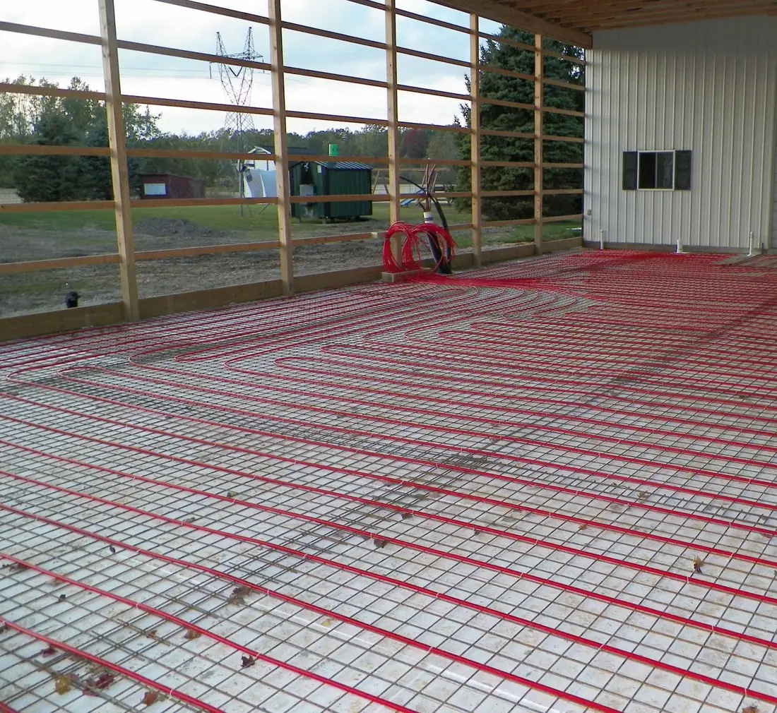 Red PEX radiant heating tubing tied to wire mesh across a pole building floor before the concrete pour