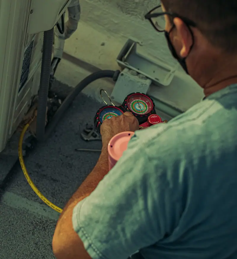 A technician reading refrigerant manifold gauges connected to an outdoor unit